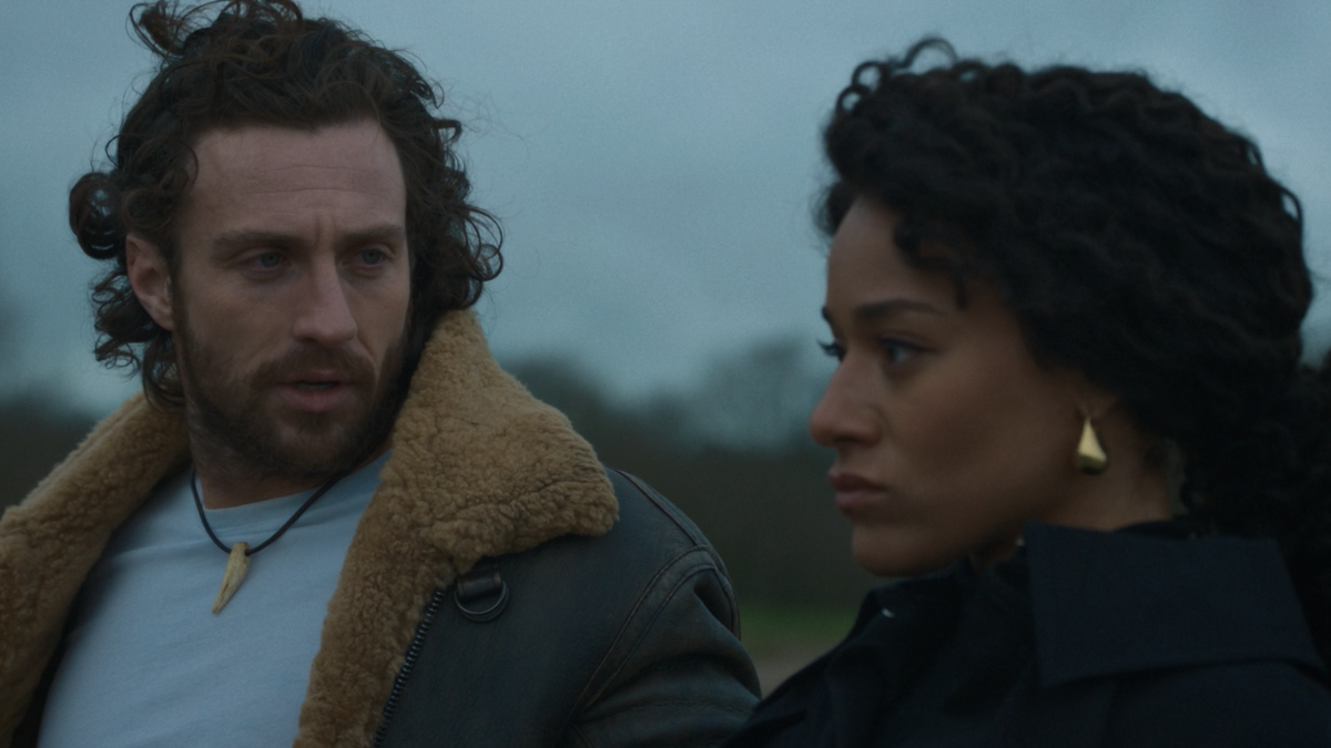 A man (Kraven) is looking at a woman (Calypso). They are on an open field.