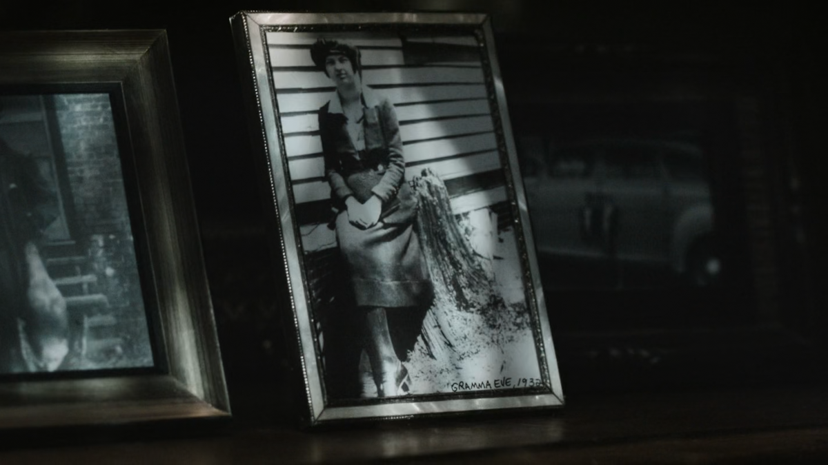 This is a framed, black and white photograph of Grandma Eve. In the picture she is holding a big leather-bound book which is The Weeping Book. There’s a writing at the bottom of the picture which says Gramma Eve, 1932.