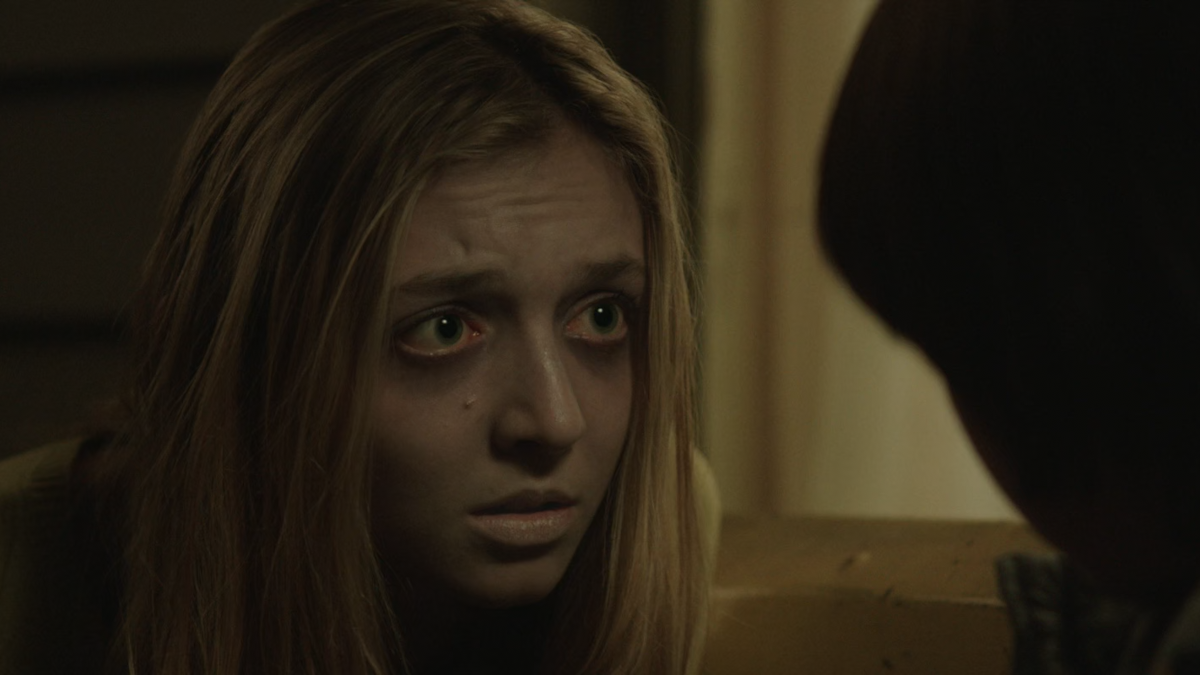 A girl is peering into George’s eyes. She looks sick. Her eyes are bloodshot and her skin is sickly, pale.