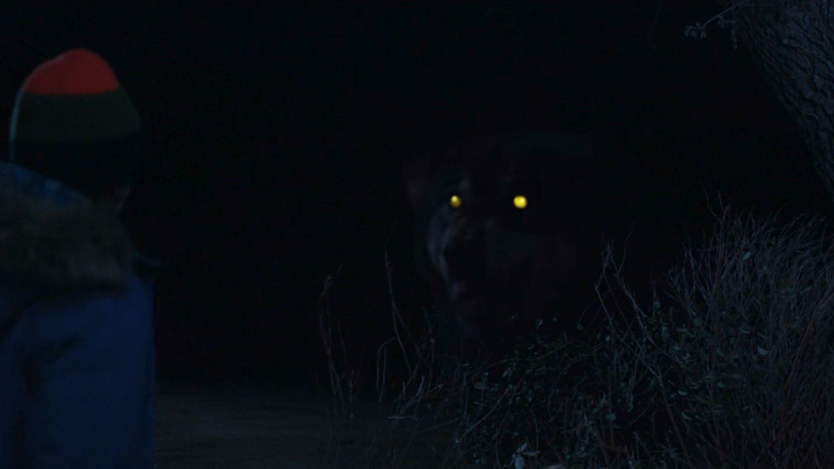 George is looking at a huge beast. There is a giant wolf with glowing eyes staring at him from the dark. It looks like it is bigger than a horse.